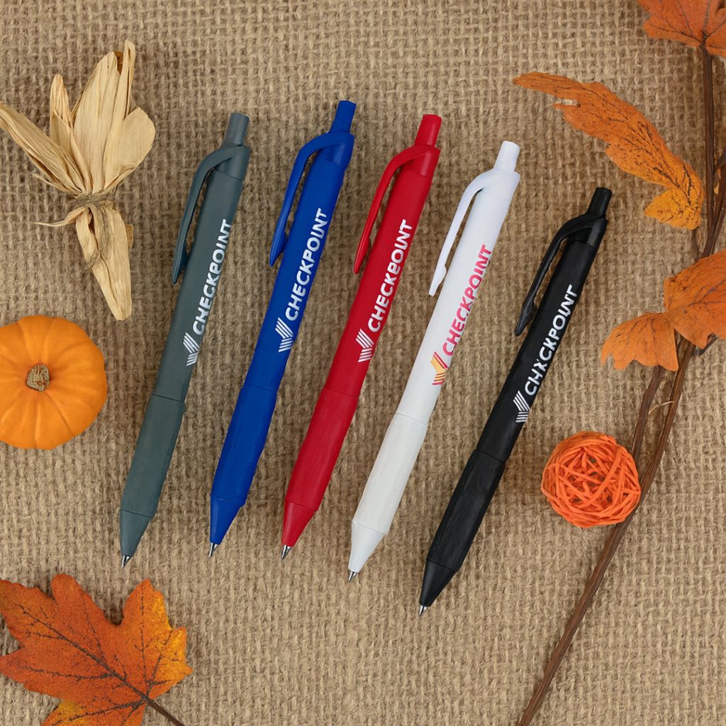 Promotional pens in multiple colors arranged on burlap with pumpkins and fall leaves.