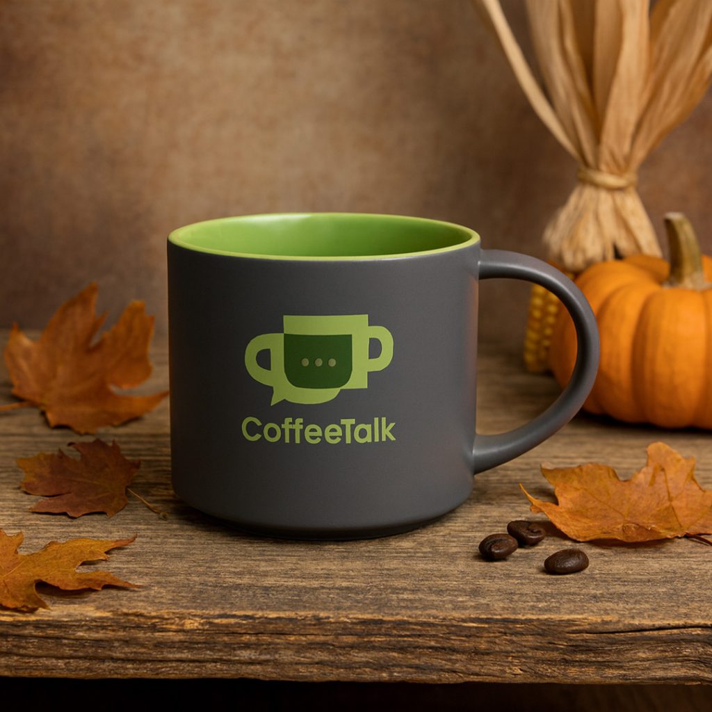 Dark gray ceramic coffee mug with green interior, surrounded by pumpkins, corn husks, and autumn leaves.
