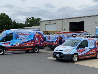 Multiple wrapped vans parked outside a warehouse for a Fredericksburg HVAC company, featuring cohesive red, white, and blue designs created by Core Prints.