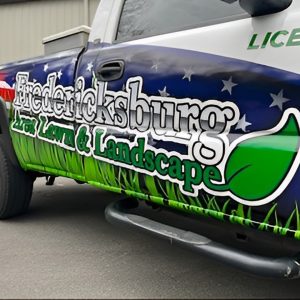 Custom vehicle wrap for Fredericksburg Lawn & Landscape featuring blue and green graphics with grass imagery and company branding applied by Core Prints.
