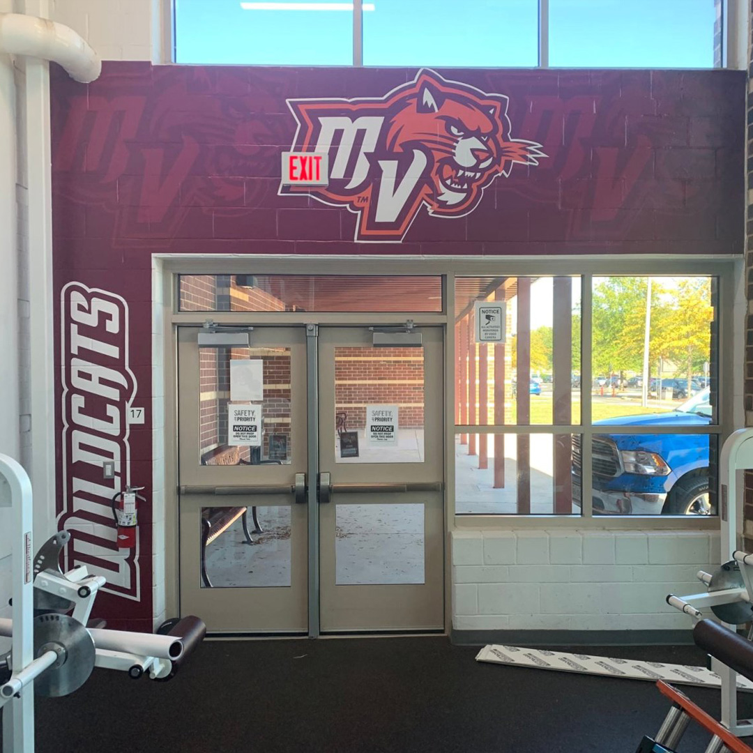 MV Wildcats gym entrance featuring a large, professionally installed wall graphic with school branding and mascot artwork.